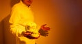 A man whose face is unrecognizable with a painted skull from the day of the dead or halloween in his hand. photograph in orange