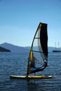 A man on a windsurf in the bay with a yacht in the background. Man learning to windsurf in the bay.