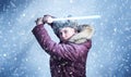 Man in winter clothes with a wooden lightsaber in his hands on a blue background with falling snow