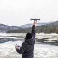 A man in a winter jacket holds a small drone in his hand. Shooting from a drone in winter