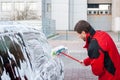 A man wipes a foam-covered black car with a brush at a self-service car wash Royalty Free Stock Photo
