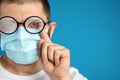 Man wiping foggy glasses caused by wearing disposable mask on background, space for text. Protective measure during
