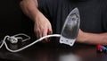 A man with wire cutters disconnects the wire from the iron. Repairing a burnt iron at home. Tools for repair are on the table