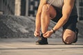 A man with wired headphones in a light athletic uniform ties a lace on a shoe for running. Sport concept