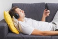 Man in wirwlwss headphones watching lying on sofa and looking on his smartphone