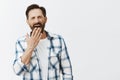 Man woke up early not be late on work, feeling sleepy and tired, standing over gray background in casual checked shirt Royalty Free Stock Photo