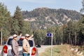 A man and a woman autotourists stand on the highway near the car and point to the high mountain Aleksandrovskaya Sopka