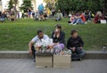 Man, woman and boy street vendors selling sweets sitting on the pavement, blurred people relaxing on a grass at the city