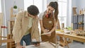A man and woman in a carpentry workshop collaboratively measure wood on a workbench Royalty Free Stock Photo