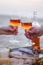 Man and woman clanging wine glasses with rose wine at sunset bea