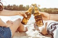 Man and woman clinking bottles of beer while resting on beach