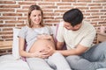 Man and woman couple touching belly sitting on bed at bedroom Royalty Free Stock Photo