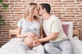 Man and woman couple touching belly sitting on bed kissing at bedroom Royalty Free Stock Photo