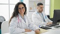 Man and woman doctors using computer taking notes smiling at the clinic