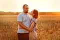A man and a woman embrace against the background of the setting sun in a wheat field. They look at each other. Lovers at sunset in