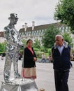 Indian couple check out motionless, silver mirrored street performer in London, England