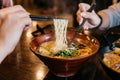 Man and woman hands pinching noodle in Ramen Pork Bone Soup Tonkotsu Ramen with Chashu Pork, Scallion, Sprout, Corn.