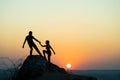 Man and woman hikers helping each other to climb a big stone at sunset in mountains. Couple climbing on a high rock in evening