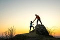 Man and woman hikers helping each other to climb a big stone at sunset in mountains. Couple climbing on a high rock in evening