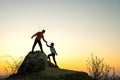 Man and woman hikers helping each other to climb a big stone at sunset in mountains. Couple climbing on a high rock in evening