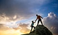 Man and woman hikers helping each other to climb a big stone at sunset in mountains. Couple climbing on a high rock in evening