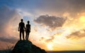 Man and woman hikers standing on a big stone at sunset in mountains. Couple together on a high rock in evening nature. Tourism, Royalty Free Stock Photo