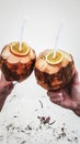 Man and woman holding coconut juice punch cocktails in hands. Close up view with white sand in the background. Serene island Royalty Free Stock Photo