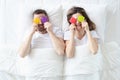 Man and woman are holding colorful condoms while lying on bed