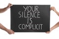 Man and woman holding sign with phrase Your Silence Is Complicit on white background, closeup. Racism concept