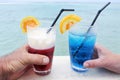 Man and woman holds a red and blue cocktail drinks with ice served over a lagoon of a tropical island resort Royalty Free Stock Photo