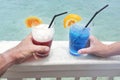 Man and woman holds a red and blue cocktail drinks with ice served over a lagoon of a tropical island resort Royalty Free Stock Photo