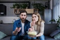 A man and a woman at home watching a boring movie, switching channels and eating popcorn Royalty Free Stock Photo