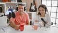 Man and woman interviewers sharing a coffee moment in a radio studio