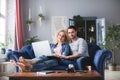 Man and woman with laptop sitting on a blue sofa at home. Young family planning Royalty Free Stock Photo
