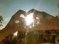 Man and woman make a heart around the sun with their hands. Male and female hand in the rays and glare of the sun makes the shape