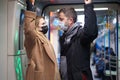 Man and woman in medical masks holding handrails in subway car