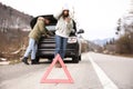 Man and woman near broken car, focus on emergency stop sign. Winter day