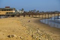 A man and a woman playing with their dog on the beach near the pier with vast blue ocean water and silky brown sand Royalty Free Stock Photo