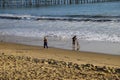 A man and a woman playing with their dog on the beach near the pier with vast blue ocean water and silky brown sand Royalty Free Stock Photo