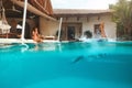 Man And Woman At Pool. Couple In Love Enjoying Summer Vacation At Tropical Villa. Male Diving In Water From Poolside.