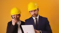 Man and woman professional architects with hard hats, tablet and walkie talkie isolated on orange background Royalty Free Stock Photo