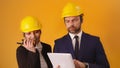 Man and woman professional architects with hard hats, tablet and walkie talkie isolated on orange background Royalty Free Stock Photo