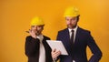 Man and woman professional architects with hard hats, tablet and walkie talkie isolated on orange background Royalty Free Stock Photo