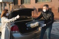 A man and a woman in protective medical masks and gloves load a suitcase into the trunk and leave the house by car Royalty Free Stock Photo