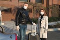 Man and woman in protective medical masks and gloves with a suitcase leave the house by car during the quarantine and Royalty Free Stock Photo