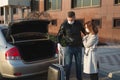 Man and woman in protective medical masks and gloves with a suitcase leave the house by car during the quarantine and Royalty Free Stock Photo