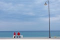 A man and a woman in red clothes are sitting on a bench against a blue sea.