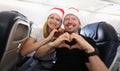 Man and woman in santa hats flying in airplane and showing heart with hands