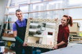 Man and woman showing a mirror with handmade wooden frame in glazier workshop