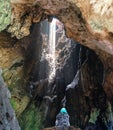 Man or Woman Sit At Big Rock and Look Up In Front of The Entrance To The Cave Where Sun Light Coming Up From Above The Cave. Royalty Free Stock Photo